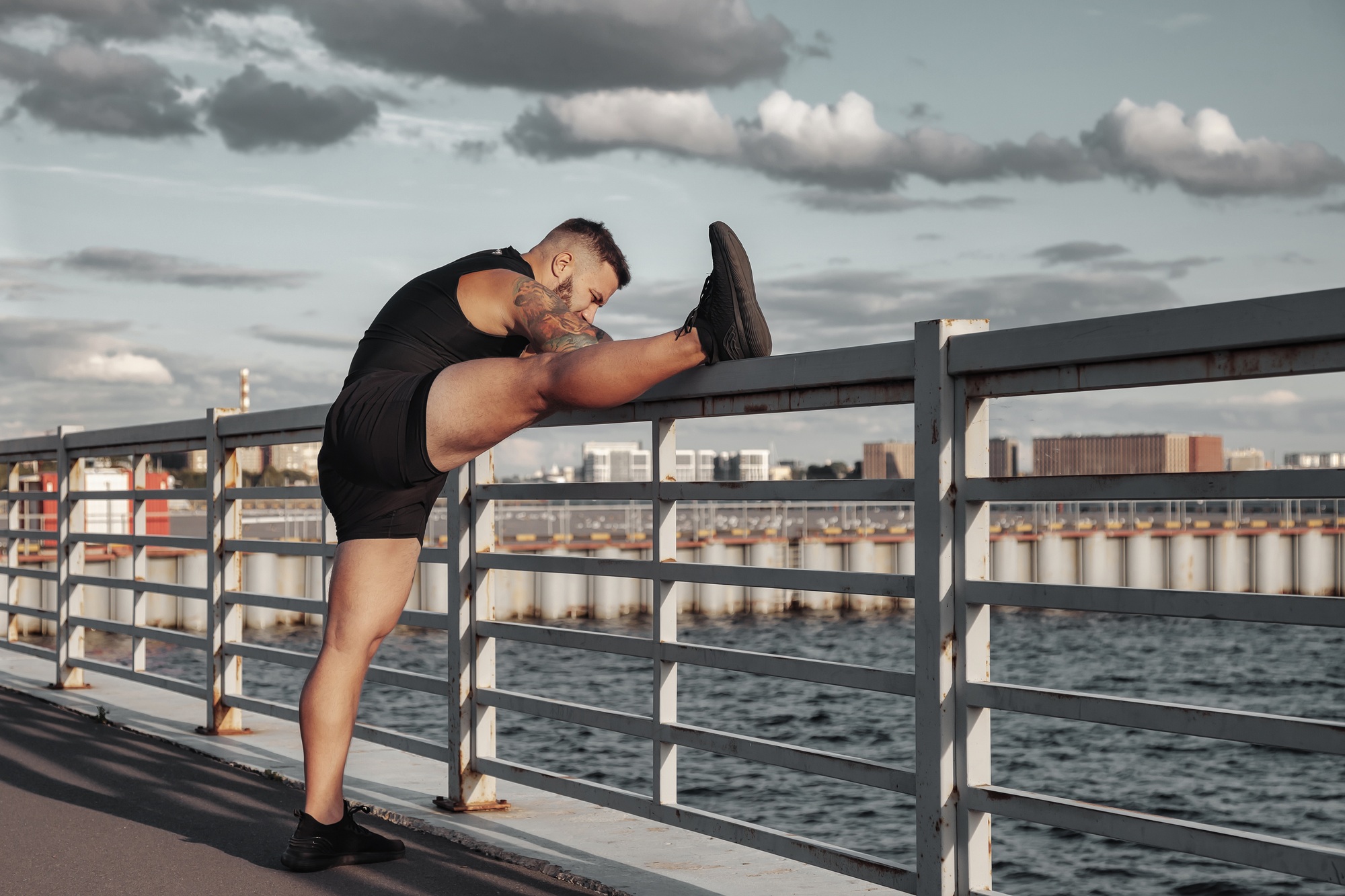 Sporty man does sports outdoors on sea embankment of city at sunset: performs exercises. Sport life